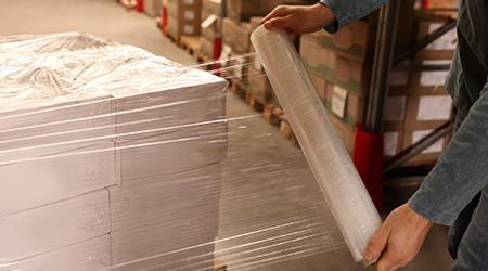 Operatore che applica film estensibile manuale trasparente su pallet di scatole in magazzino